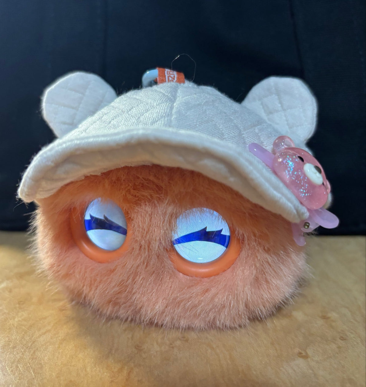 Orange Fuzozo wearing a white bear-ear cap